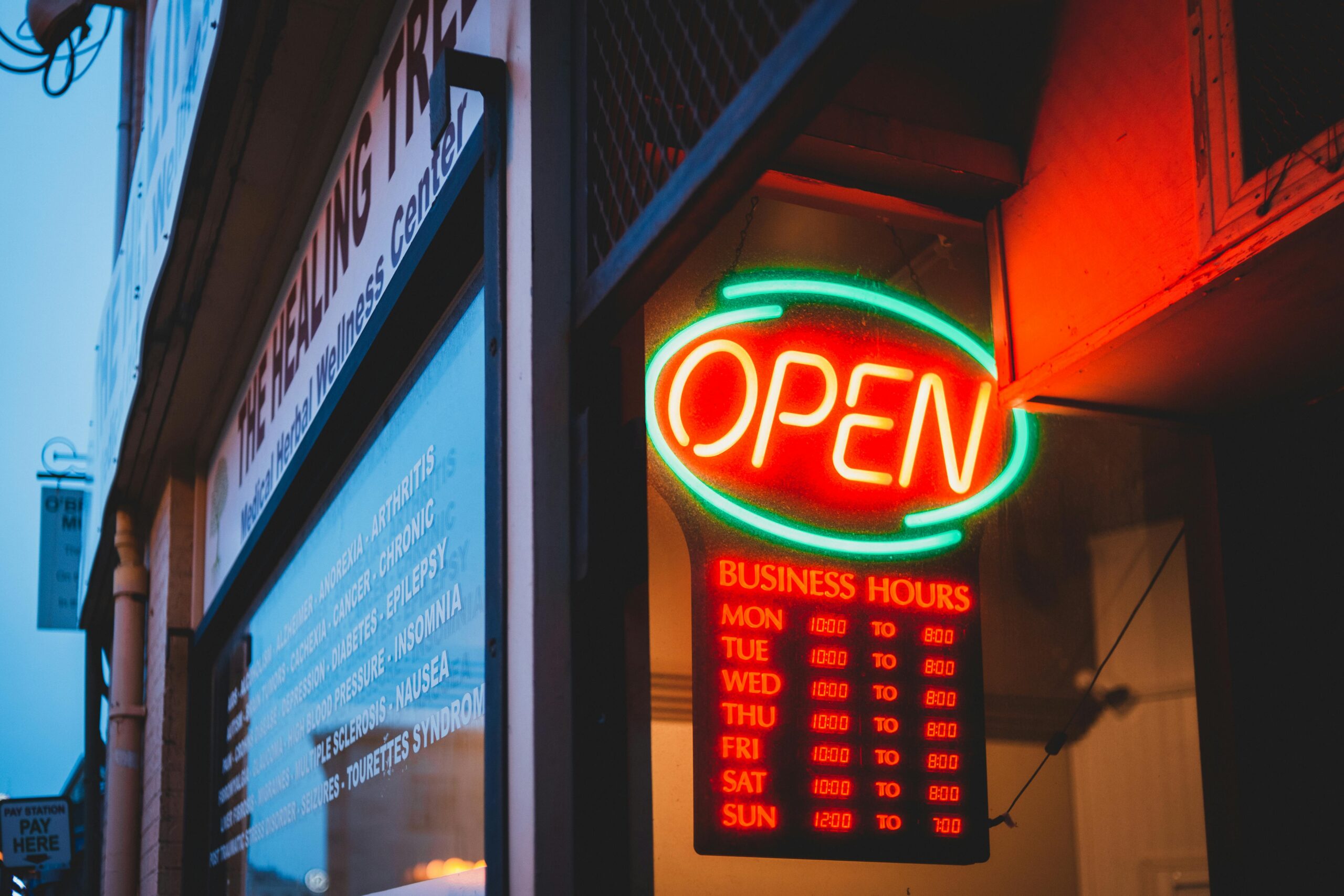 Colorful glowing neon signboard with word open and timetable on urban avenue in late evening